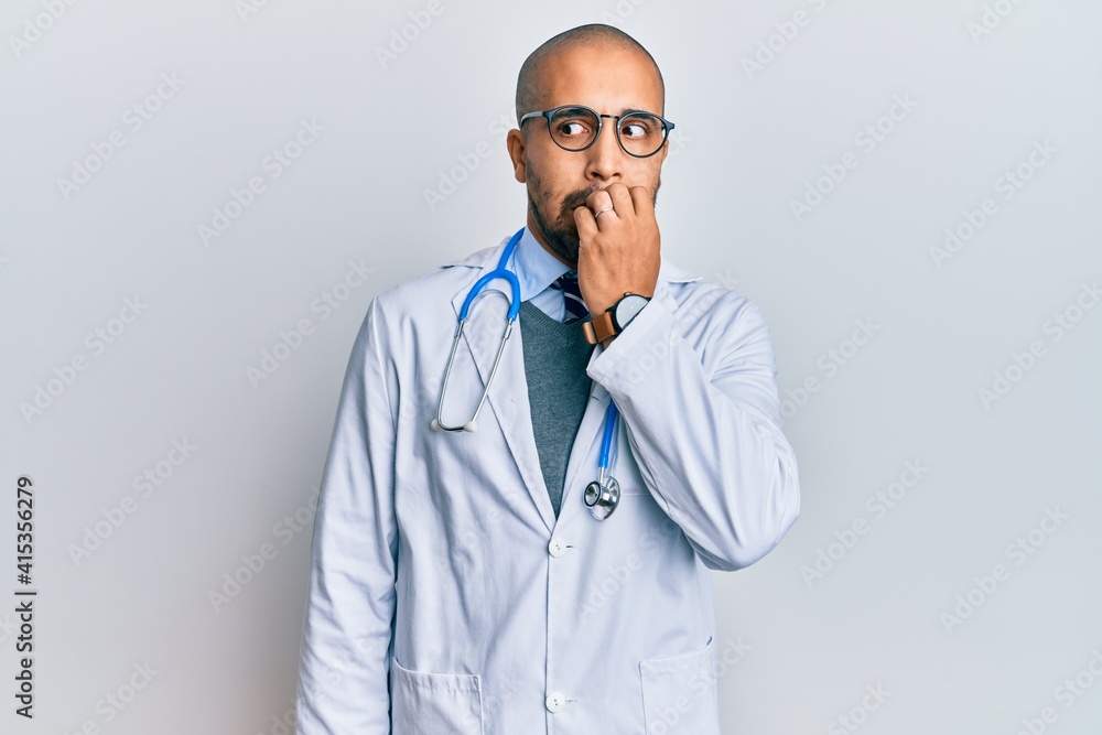 Hispanic adult man wearing doctor uniform and stethoscope looking stressed and nervous with hands on mouth biting nails. anxiety problem. Hispanic adult man wearing doctor uniform and stethoscope looking stressed and nervous with hands on mouth biting nails. anxiety problem.