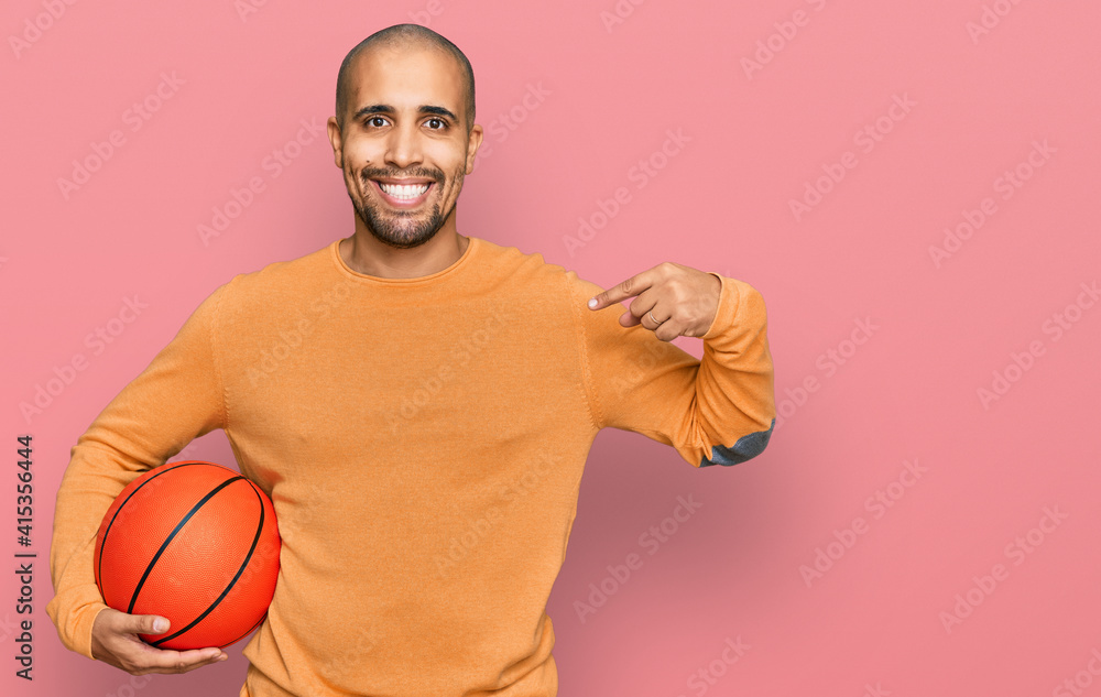 Hispanic adult man holding basketball ball pointing finger to one self smiling happy and proud Hispanic adult man holding basketball ball pointing finger to one self smiling happy and proud