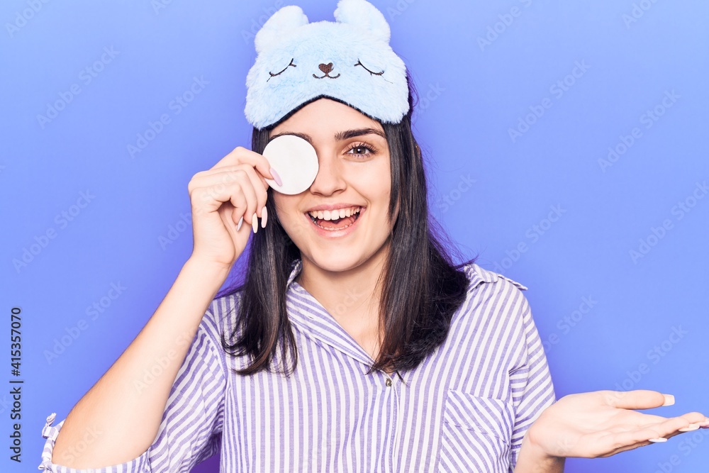 Young beautiful girl wearing funny sleep mask using makeup remover cotton celebrating achievement with happy smile and winner expression with raised hand Young beautiful girl wearing funny sleep mask using makeup remover cotton celebrating achievement with happy smile and winner expression with raised hand