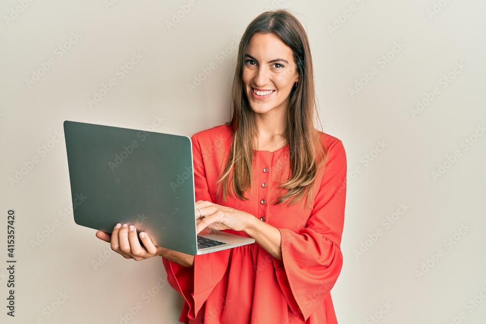 Young beautiful woman working using computer laptop looking positive and happy standing and smiling with a confident smile showing teeth Young beautiful woman working using computer laptop looking positive and happy standing and smiling with a confident smile showing teeth