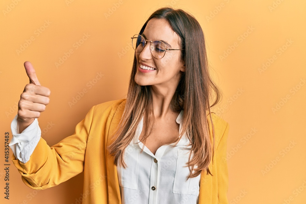 Young beautiful woman wearing business style and glasses looking proud, smiling doing thumbs up gesture to the side Young beautiful woman wearing business style and glasses looking proud, smiling doing thumbs up gesture to the side