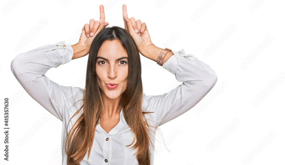 Young beautiful woman wearing casual clothes doing funny gesture with finger over head as bull horns Young beautiful woman wearing casual clothes doing funny gesture with finger over head as bull horns