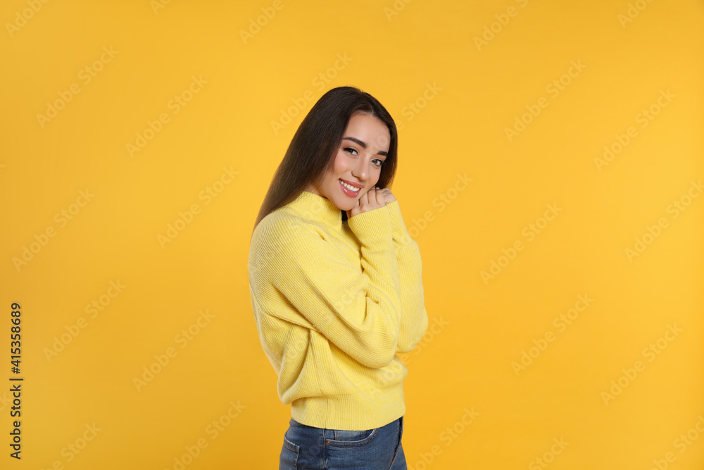 Beautiful young woman wearing warm sweater on yellow background Beautiful young woman wearing warm sweater on yellow background