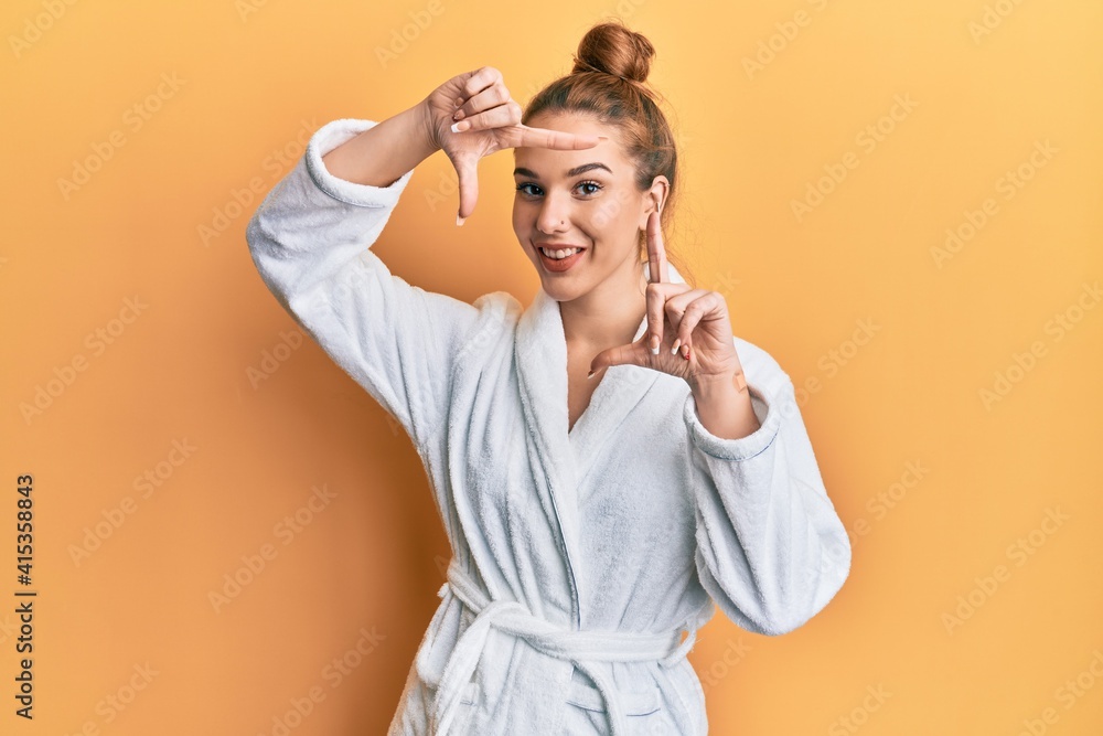 Young blonde woman wearing bathrobe smiling making frame with hands and fingers with happy face. creativity and photography concept. Young blonde woman wearing bathrobe smiling making frame with hands and fingers with happy face. creativity and photography concept.