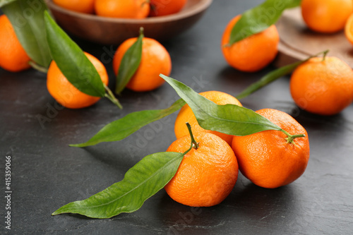 Fresh tangerines with green leaves on black table