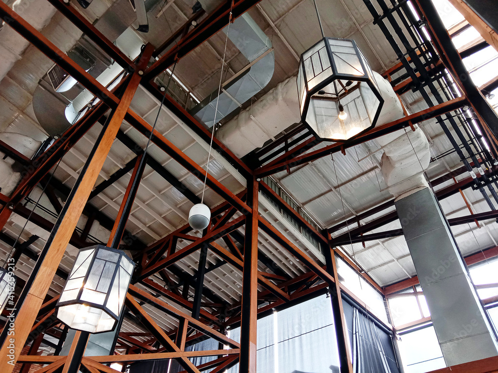 Construction of a large wooden roof and decorative lights. Wooden ceiling. Home and shopping Mall interior concept. Glass lantern hanging on wooden roof frames. Construction of a large wooden roof and decorative lights. Wooden ceiling. Home and shopping Mall interior concept. Glass lantern hanging on wooden roof frames.