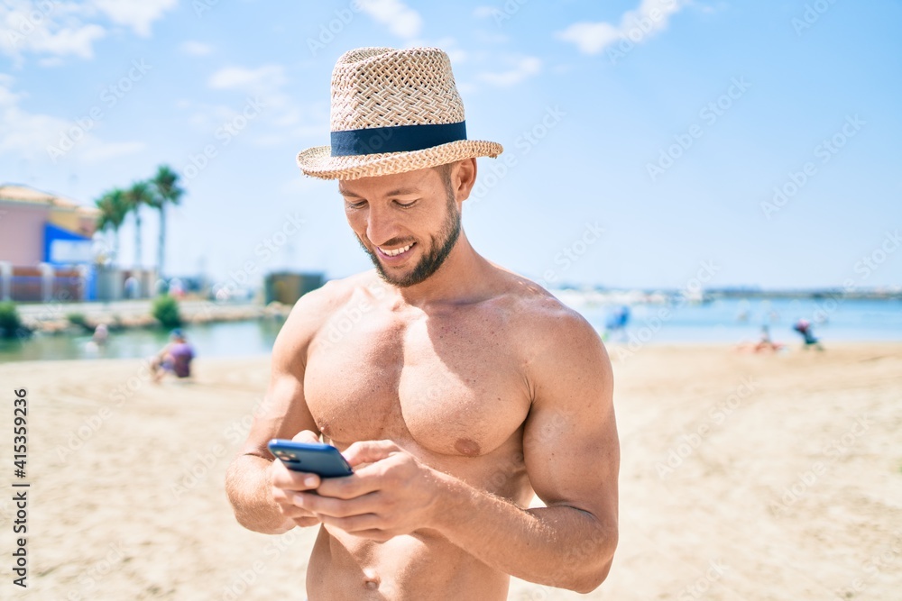 Handsome fitness caucasian man at the beach on a sunny day wearing summer hat