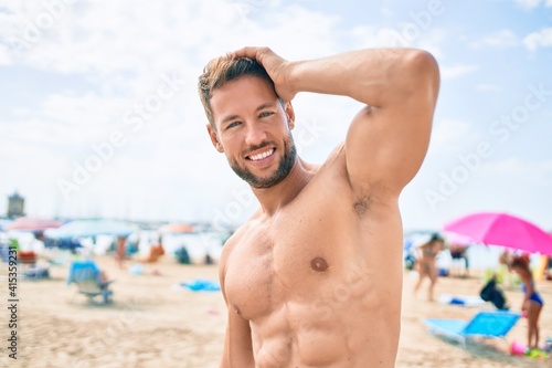 Handsome fitness caucasian man at the beach on a sunny day showing muscular fitness body