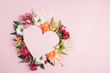 Heart surrounded with fresh colorful flowers on pastel pink background. Creative love layout with copy space. Valentines day, wedding or romantic visual trend. Spring bloom. Flat lay.