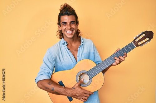 Young hispanic man playing classical guitar smiling with a happy and cool smile on face. showing teeth.