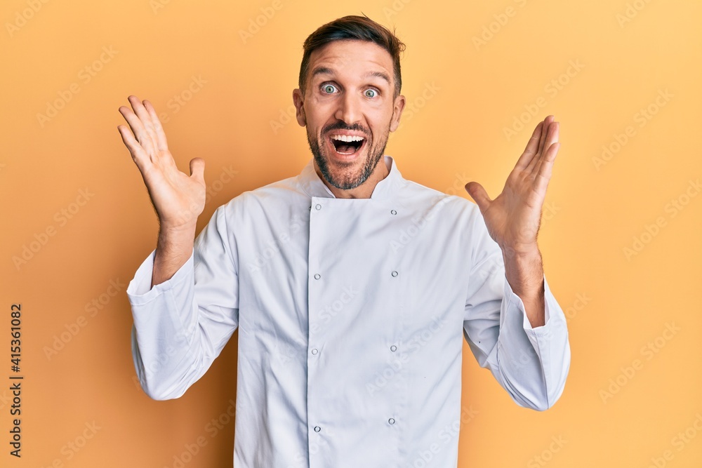 Handsome man with beard wearing professional cook uniform celebrating crazy and amazed for success with arms raised and open eyes screaming excited. winner concept Handsome man with beard wearing professional cook uniform celebrating crazy and amazed for success with arms raised and open eyes screaming excited. winner concept