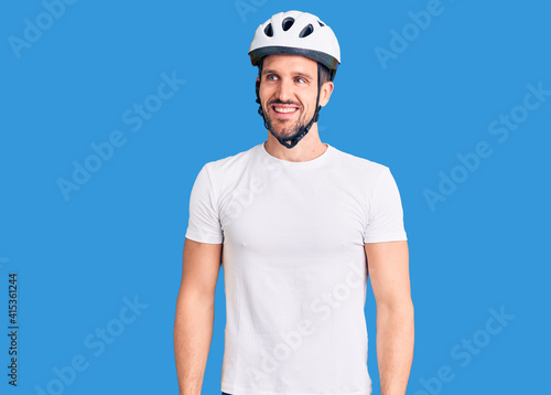 Young handsome man wearing bike helmet looking away to side with smile on face, natural expression. laughing confident.