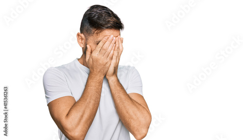 Handsome man with beard wearing casual white t shirt with sad expression covering face with hands while crying. depression concept.