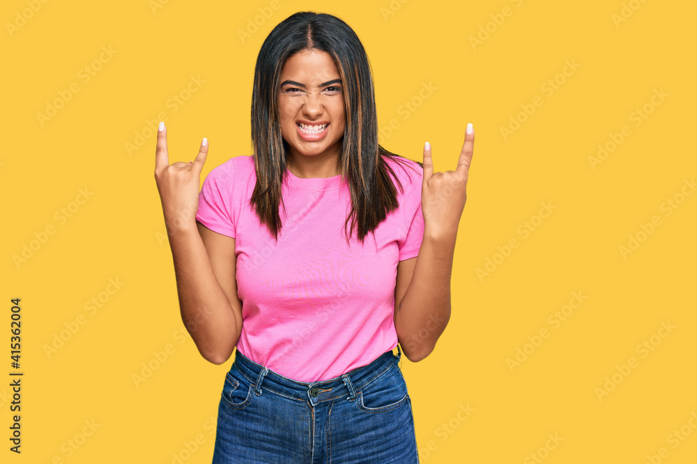 Young latin girl wearing casual clothes shouting with crazy expression doing rock symbol with hands up. music star. heavy concept. Young latin girl wearing casual clothes shouting with crazy expression doing rock symbol with hands up. music star. heavy concept.