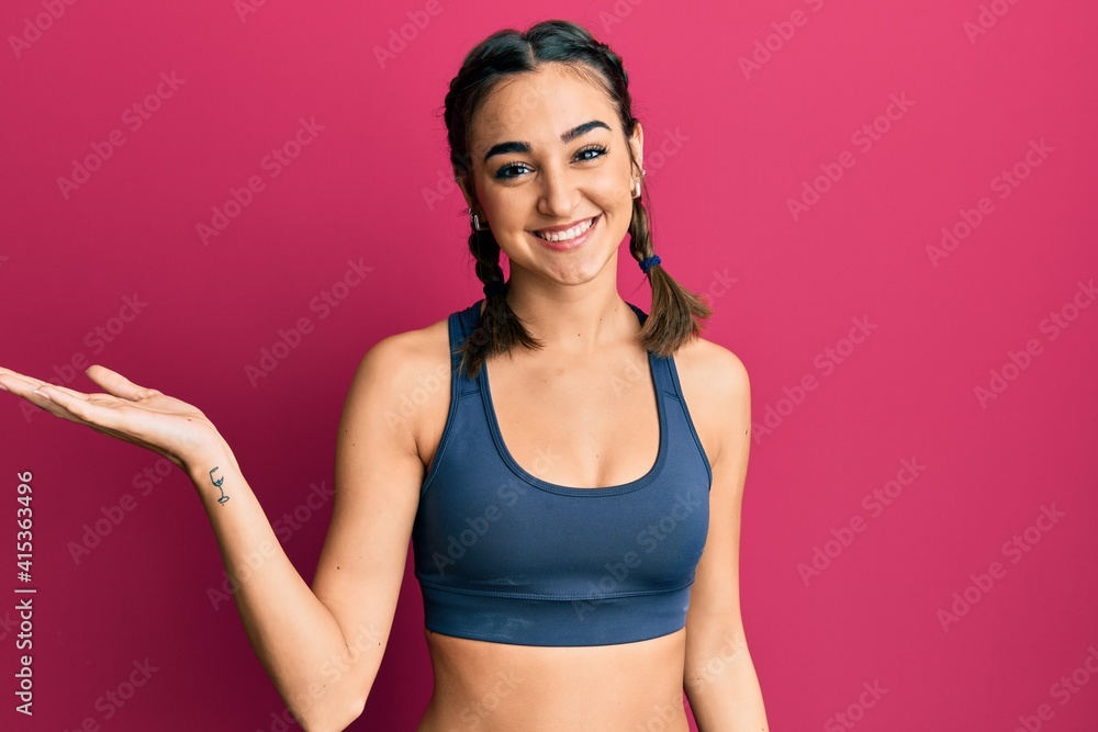 Young brunette girl wearing sportswear and braids smiling cheerful presenting and pointing with palm of hand looking at the camera.