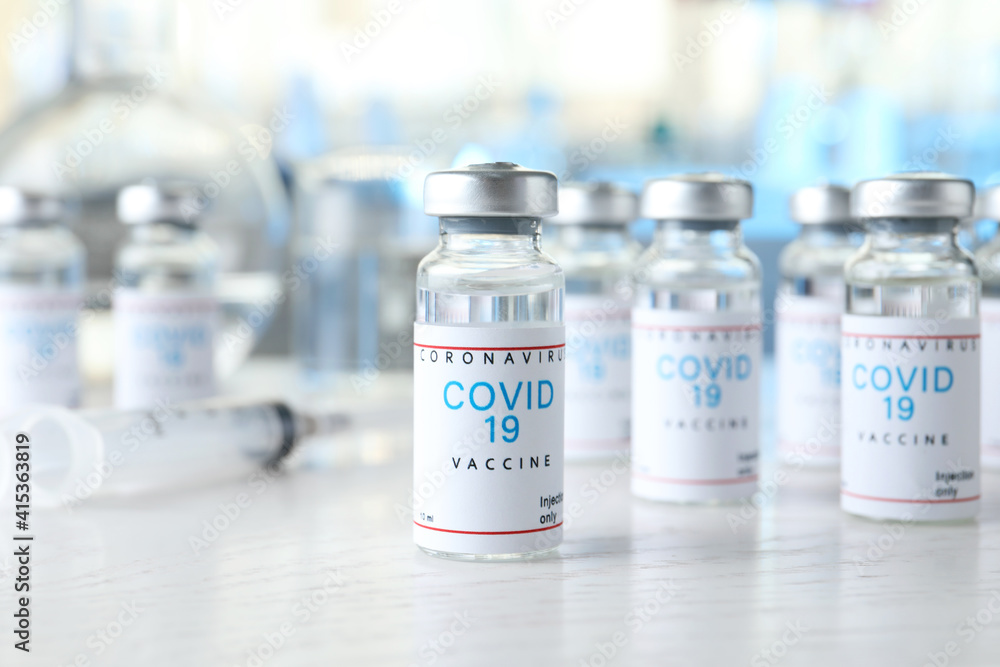 Glass vials with COVID-19 vaccine on white wooden table Glass vials with COVID-19 vaccine on white wooden table