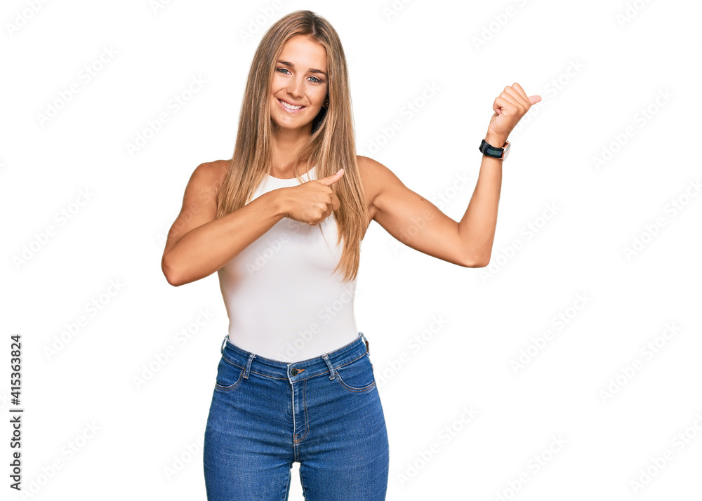 Young blonde woman wearing casual style with sleeveless shirt pointing to the back behind with hand and thumbs up, smiling confident Young blonde woman wearing casual style with sleeveless shirt pointing to the back behind with hand and thumbs up, smiling confident