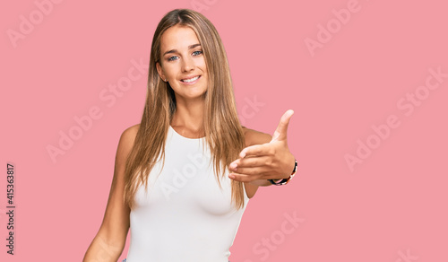 Young blonde woman wearing casual style with sleeveless shirt smiling friendly offering handshake as greeting and welcoming. successful business.