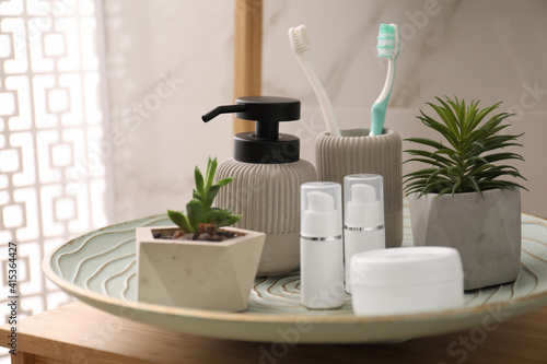 Holder with toothbrushes, different toiletries and plants on wooden table in bathroom, closeup
