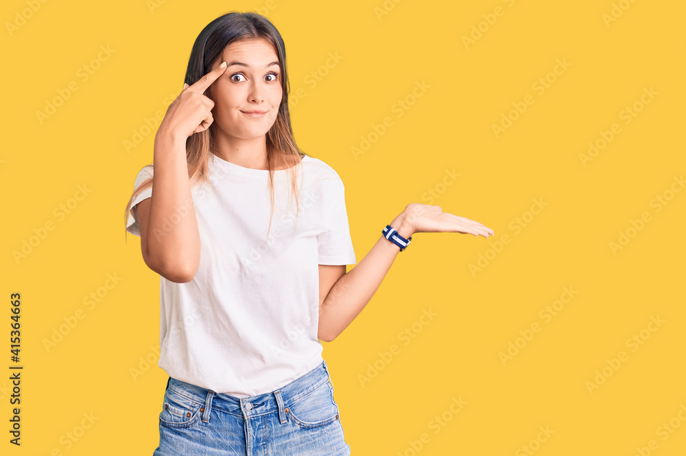 Beautiful caucasian woman wearing casual white tshirt confused and annoyed with open palm showing copy space and pointing finger to forehead. think about it. Beautiful caucasian woman wearing casual white tshirt confused and annoyed with open palm showing copy space and pointing finger to forehead. think about it.