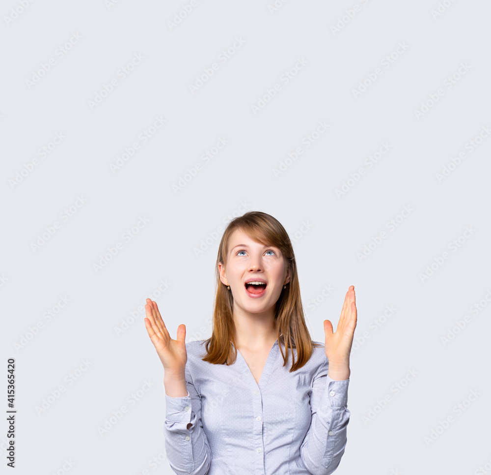 Caucasian cute, nice, office manager. Blonde woman pointing up at empty space to show you needed information isolated over grey color background. Surprised face with opened mouth Caucasian cute, nice, office manager. Blonde woman pointing up at empty space to show you needed information isolated over grey color background. Surprised face with opened mouth