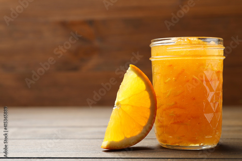 Delicious orange marmalade and citrus fruit slice on wooden table, closeup. Space for text