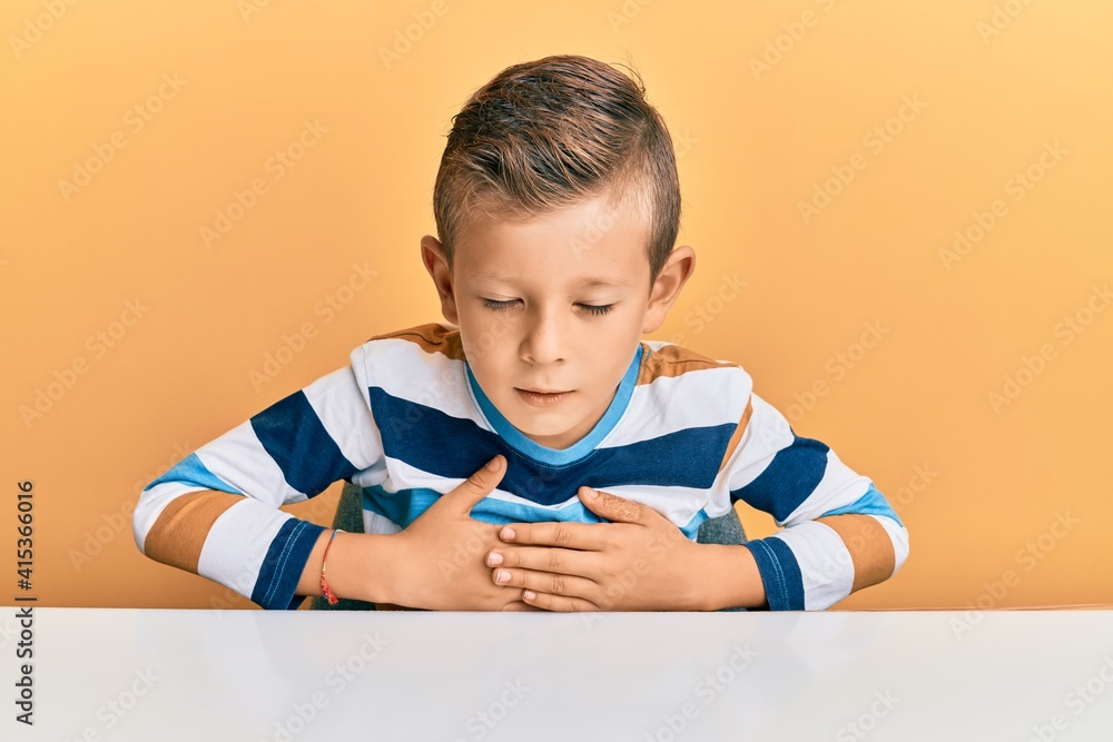 Adorable caucasian kid wearing casual clothes sitting on the table with hand on stomach because indigestion, painful illness feeling unwell. ache concept. Adorable caucasian kid wearing casual clothes sitting on the table with hand on stomach because indigestion, painful illness feeling unwell. ache concept.