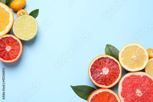 Fresh juicy citrus fruits with green leaves on light blue background  flat lay. Space for text