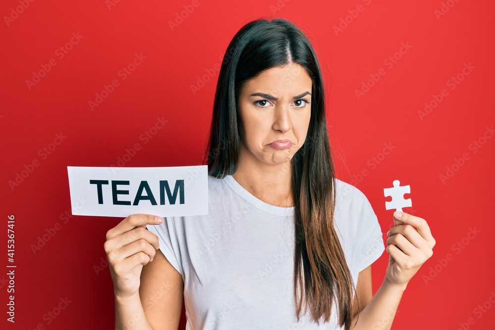Young brunette woman holding team paper and piece of puzzle as teamwork depressed and worry for distress, crying angry and afraid. sad expression. Young brunette woman holding team paper and piece of puzzle as teamwork depressed and worry for distress, crying angry and afraid. sad expression.