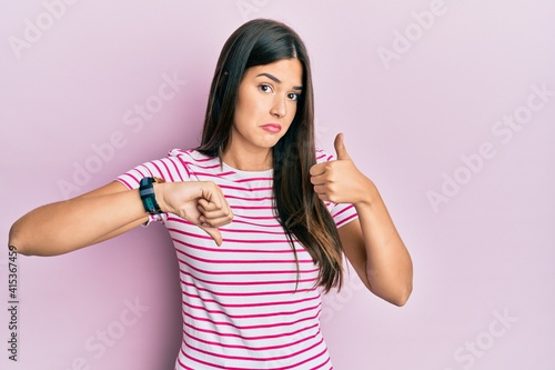 Young brunette woman wearing casual clothes over pink background doing thumbs up and down, disagreement and agreement expression. crazy conflict