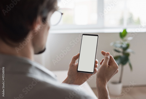 Smartphone mockup. Close up of young man hand holding phone with white blank screen at home. Isolated on white background. Mobile phone frameless design concept