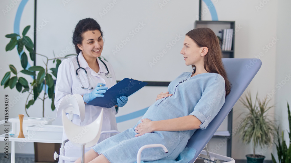 Obraz premium Happy Pregnant Woman Visit Gynecologist Doctor at the Medical Clinic. Female Doctor Examine Pregnant Young Mother to Check Up Her Healthcare. Teenage Pregnancy. Consulting of Pregnant at Clinic.