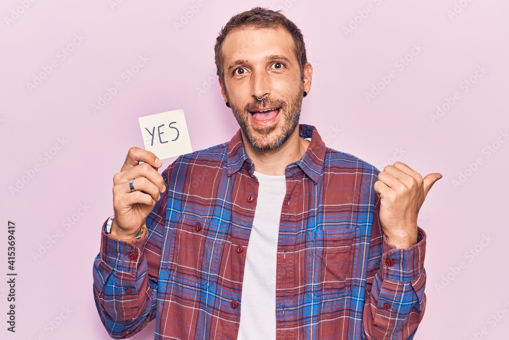 Naklejka premium Young handsome man holding yes reminder pointing thumb up to the side smiling happy with open mouth