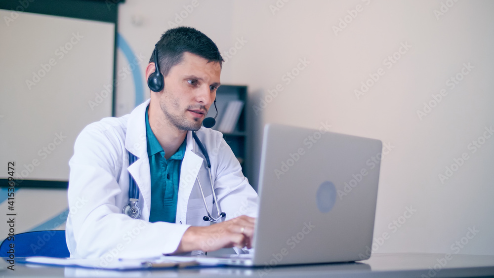 Friendly Male Doctor in White Medical Coat With Headphones Making Conference Call on Laptop.Remote Consulting Patient Online From Healthcare Hospital. Telemedicine. Friendly Male Doctor in White Medical Coat With Headphones Making Conference Call on Laptop.Remote Consulting Patient Online From Healthcare Hospital. Telemedicine.