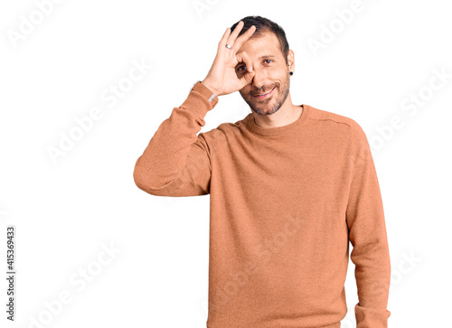 Young handsome man wearing casual clothes doing ok gesture with hand smiling, eye looking through fingers with happy face.