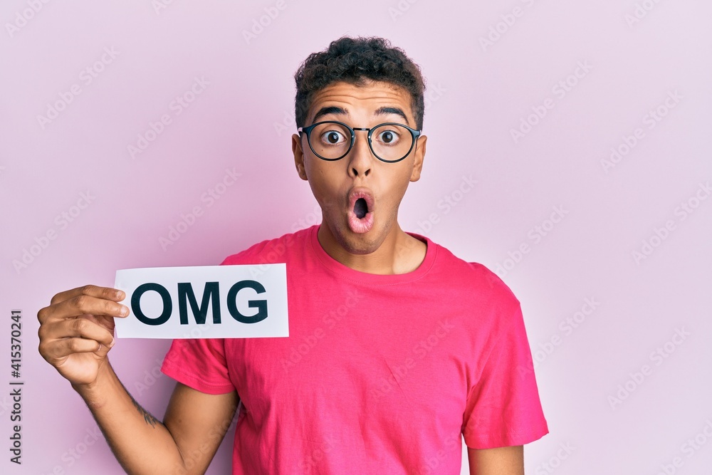 Young handsome african american man holding omg message paper scared and amazed with open mouth for surprise, disbelief face Young handsome african american man holding omg message paper scared and amazed with open mouth for surprise, disbelief face