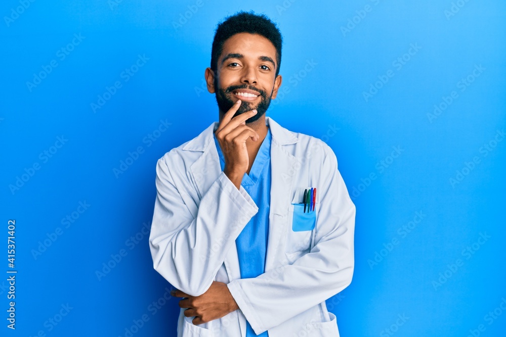 Handsome hispanic man with beard wearing doctor uniform looking confident at the camera with smile with crossed arms and hand raised on chin. thinking positive. Handsome hispanic man with beard wearing doctor uniform looking confident at the camera with smile with crossed arms and hand raised on chin. thinking positive.