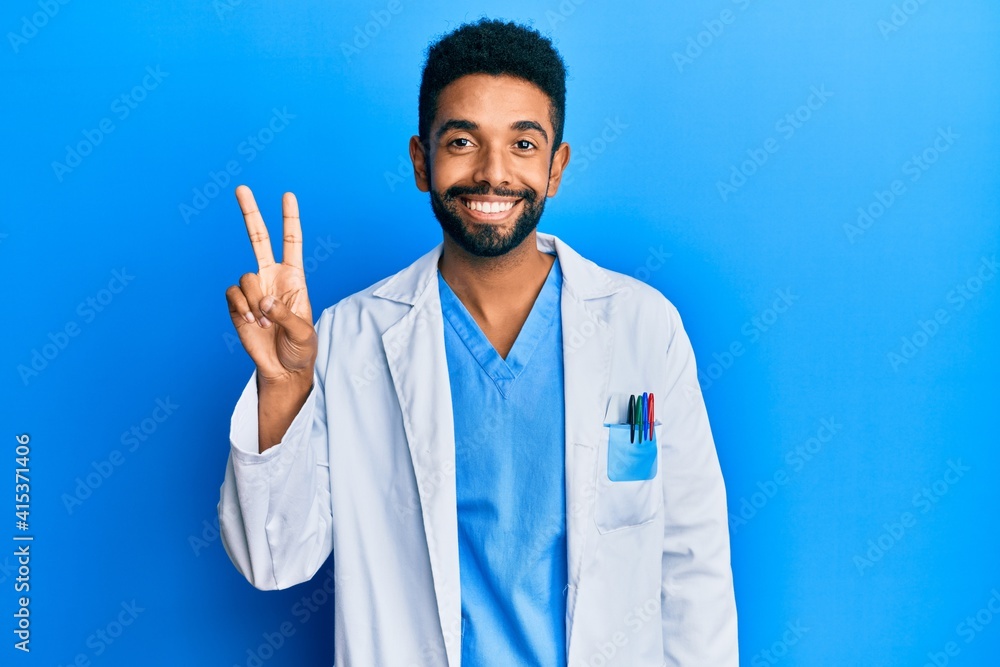 Handsome hispanic man with beard wearing doctor uniform showing and pointing up with fingers number two while smiling confident and happy. Handsome hispanic man with beard wearing doctor uniform showing and pointing up with fingers number two while smiling confident and happy.