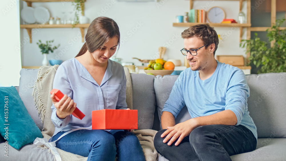 Ordering Gifts Online. A Man Gives a Woman a Gift that He Ordered Through the Site, an Online Store. The Girl Takes Out a Red Gift From a Cardboard Box. Happy Family Time. Enjoy Each Other.