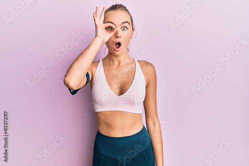 Beautiful blonde woman wearing sportswear and arm band doing ok gesture shocked with surprised face, eye looking through fingers. unbelieving expression. © Krakenimages.com