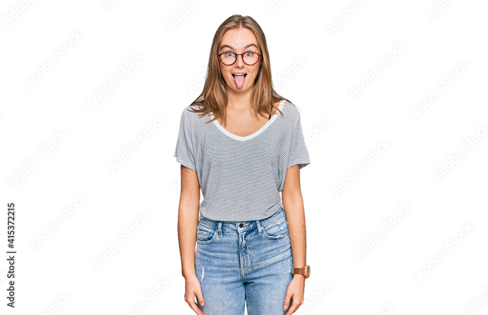 Beautiful young blonde woman wearing casual clothes and glasses sticking tongue out happy with funny expression. emotion concept. Beautiful young blonde woman wearing casual clothes and glasses sticking tongue out happy with funny expression. emotion concept.