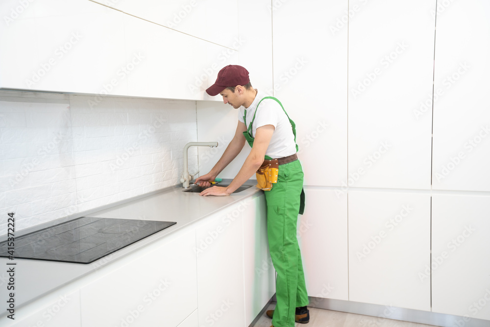 smiling adult repairman with spanner repairing faucet at kitchen smiling adult repairman with spanner repairing faucet at kitchen