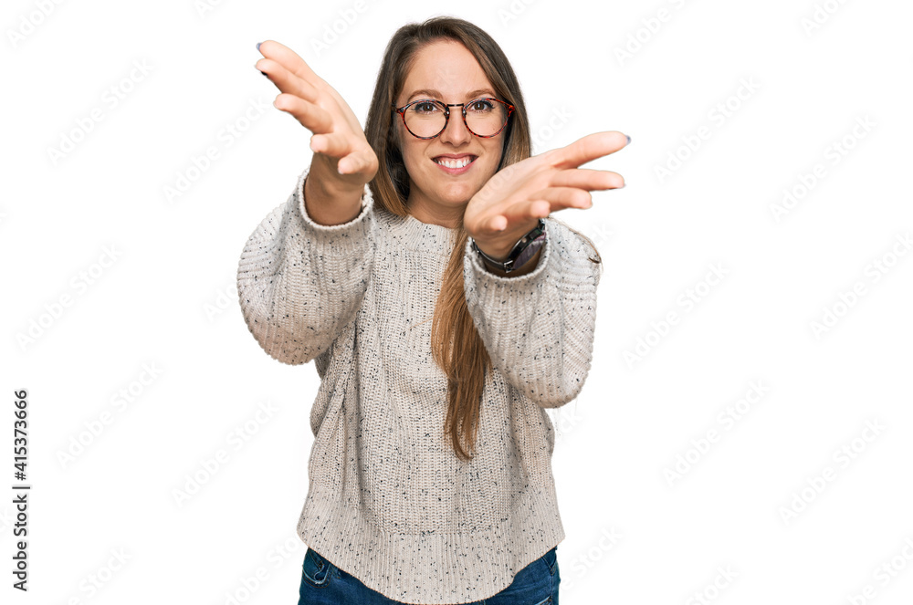 Young blonde woman wearing casual sweater and glasses looking at the camera smiling with open arms for hug. cheerful expression embracing happiness. Young blonde woman wearing casual sweater and glasses looking at the camera smiling with open arms for hug. cheerful expression embracing happiness.