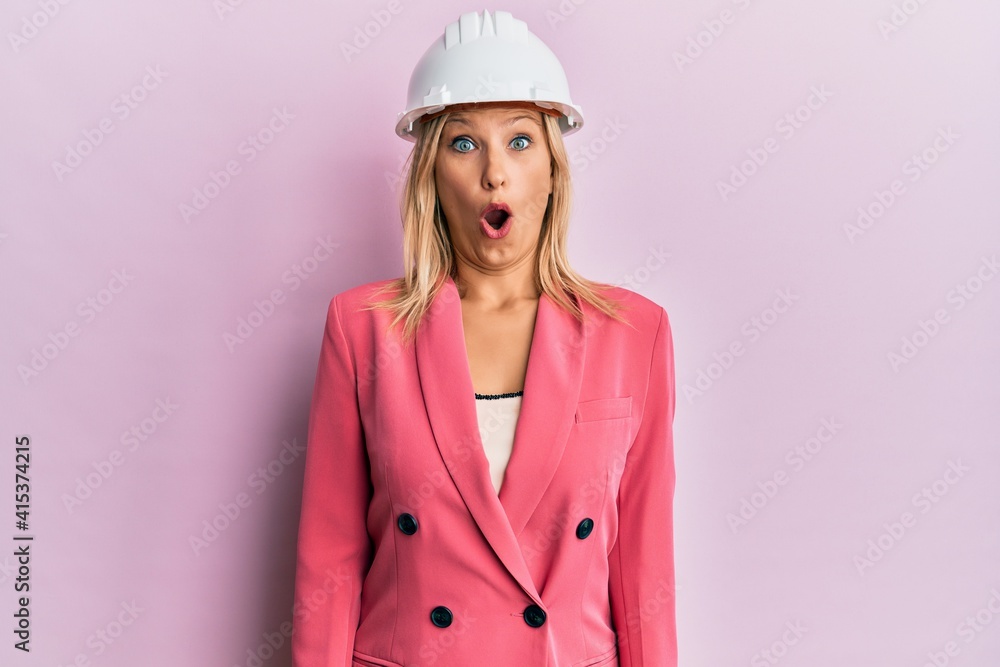 Beautiful middle age blonde woman wearing architect hardhat scared and amazed with open mouth for surprise, disbelief face