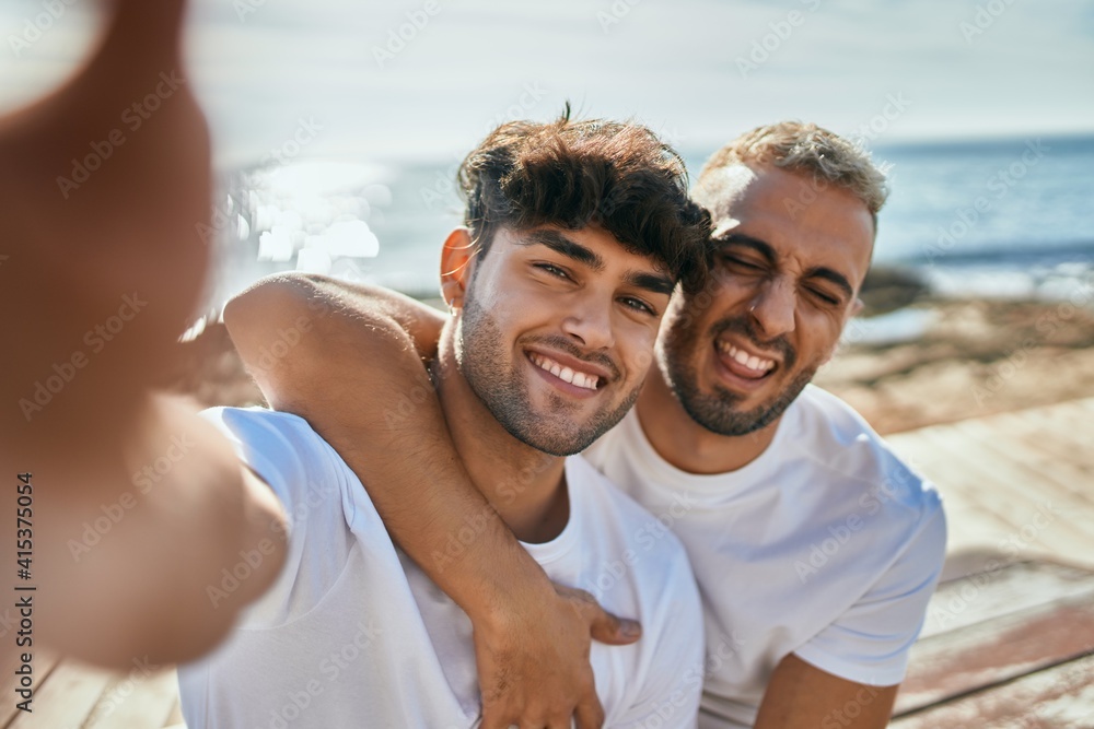 Young gay couple smiling happy making selfie by the smartphone at the beach. Young gay couple smiling happy making selfie by the smartphone at the beach.