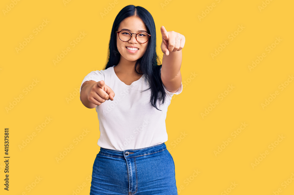 Young beautiful asian girl wearing casual clothes and glasses pointing to you and the camera with fingers, smiling positive and cheerful Young beautiful asian girl wearing casual clothes and glasses pointing to you and the camera with fingers, smiling positive and cheerful