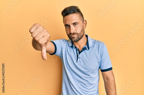 Handsome man with beard wearing casual clothes looking unhappy and angry showing rejection and negative with thumbs down gesture. bad expression.