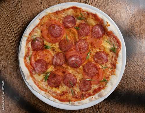 Pepperoni pizza with sausage, tomatoes and rosemary on a white plate