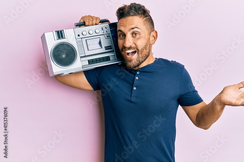 Handsome man with beard holding boombox, listening to music celebrating achievement with happy smile and winner expression with raised hand