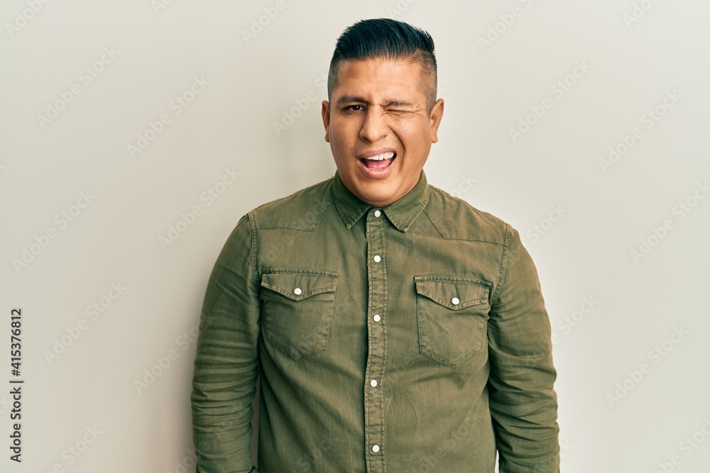 Young latin man wearing casual clothes winking looking at the camera with sexy expression, cheerful and happy face. Young latin man wearing casual clothes winking looking at the camera with sexy expression, cheerful and happy face.
